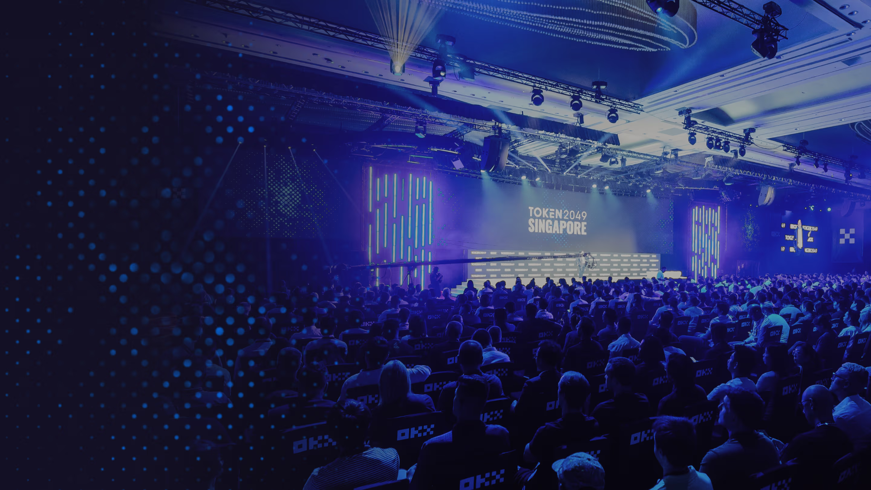 Crowd of attendees at a technology conference with a stage displaying 'TOKEN2049 SINGAPORE'.